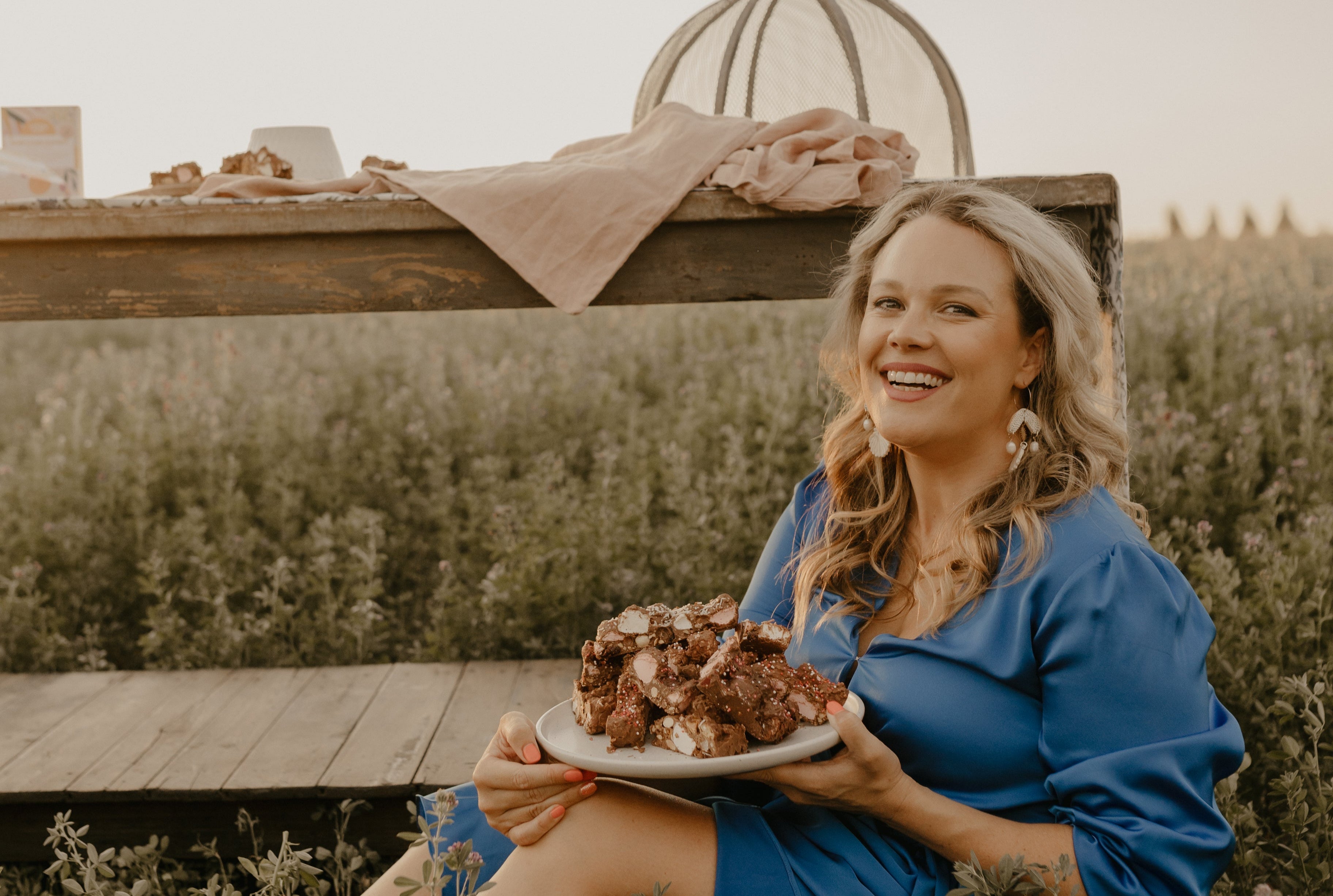 Woman in a blue dress sitting outdoors holding a plate of food.