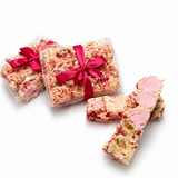 Gift-wrapped Raspberry Roundabout rocky road beside sliced white chocolate rocky road pieces with raspberries and marshmallows.