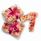 Gift-wrapped Raspberry Roundabout rocky road beside sliced white chocolate rocky road pieces with raspberries and marshmallows.