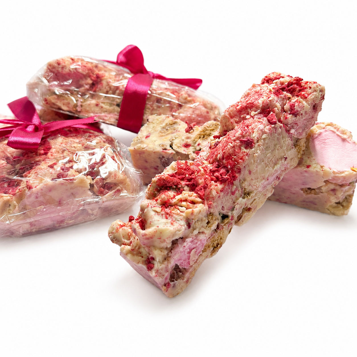 Gift-wrapped Raspberry Roundabout rocky road beside sliced white chocolate rocky road pieces with raspberries and marshmallows.