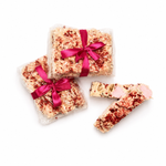 Gift-wrapped Raspberry Roundabout rocky road beside sliced white chocolate rocky road pieces with raspberries and marshmallows.