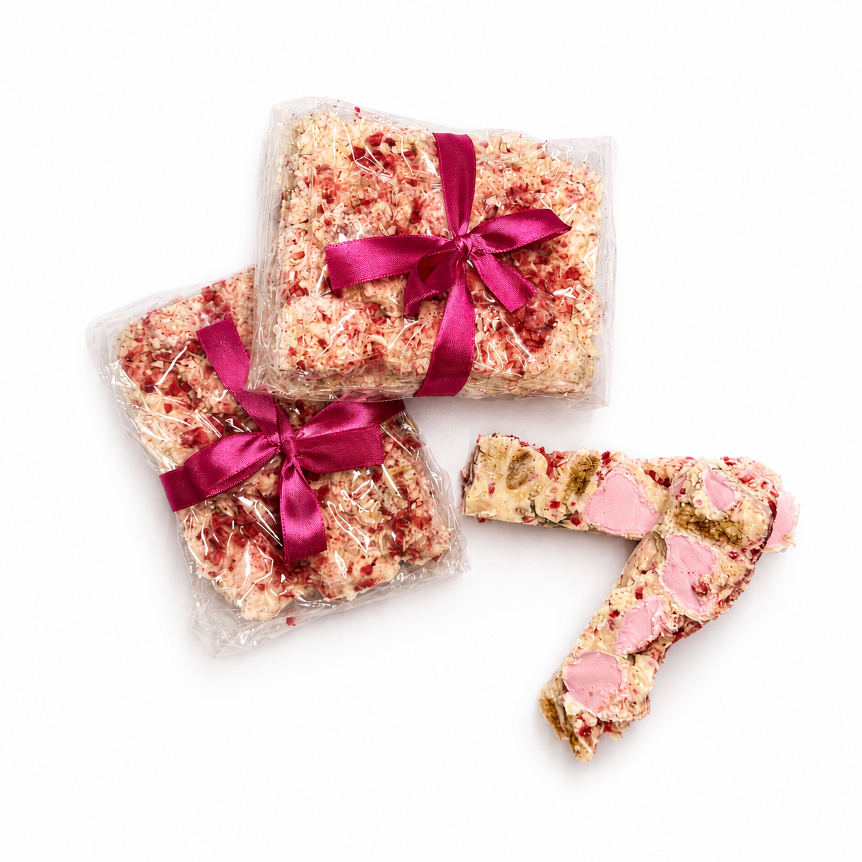 Gift-wrapped Raspberry Roundabout rocky road beside sliced white chocolate rocky road pieces with raspberries and marshmallows.