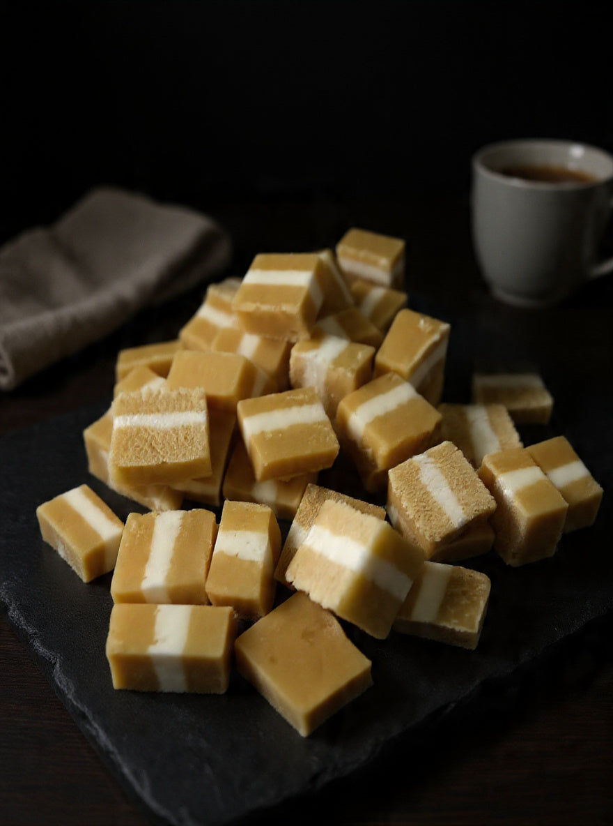 Jersey Caramels with layered caramel and creamy white filling displayed on a dark serving board with a warm drink in the background