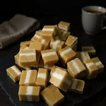 Jersey Caramels with layered caramel and creamy white filling displayed on a dark serving board with a warm drink in the background
