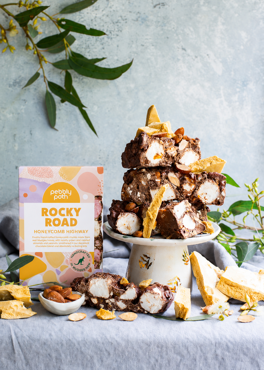 Pebbly Path Honeycomb Highway Rocky Road 200g box displayed with chunky rocky road pieces, honeycomb shards, marshmallows, roasted almonds, and native greenery on a styled dessert setting.