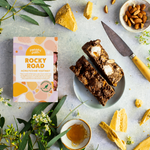 Pebbly Path Honeycomb Highway Rocky Road 200g box styled with sliced rocky road bars, honeycomb pieces, almonds, honey drizzle, and native greenery on a textured tabletop.