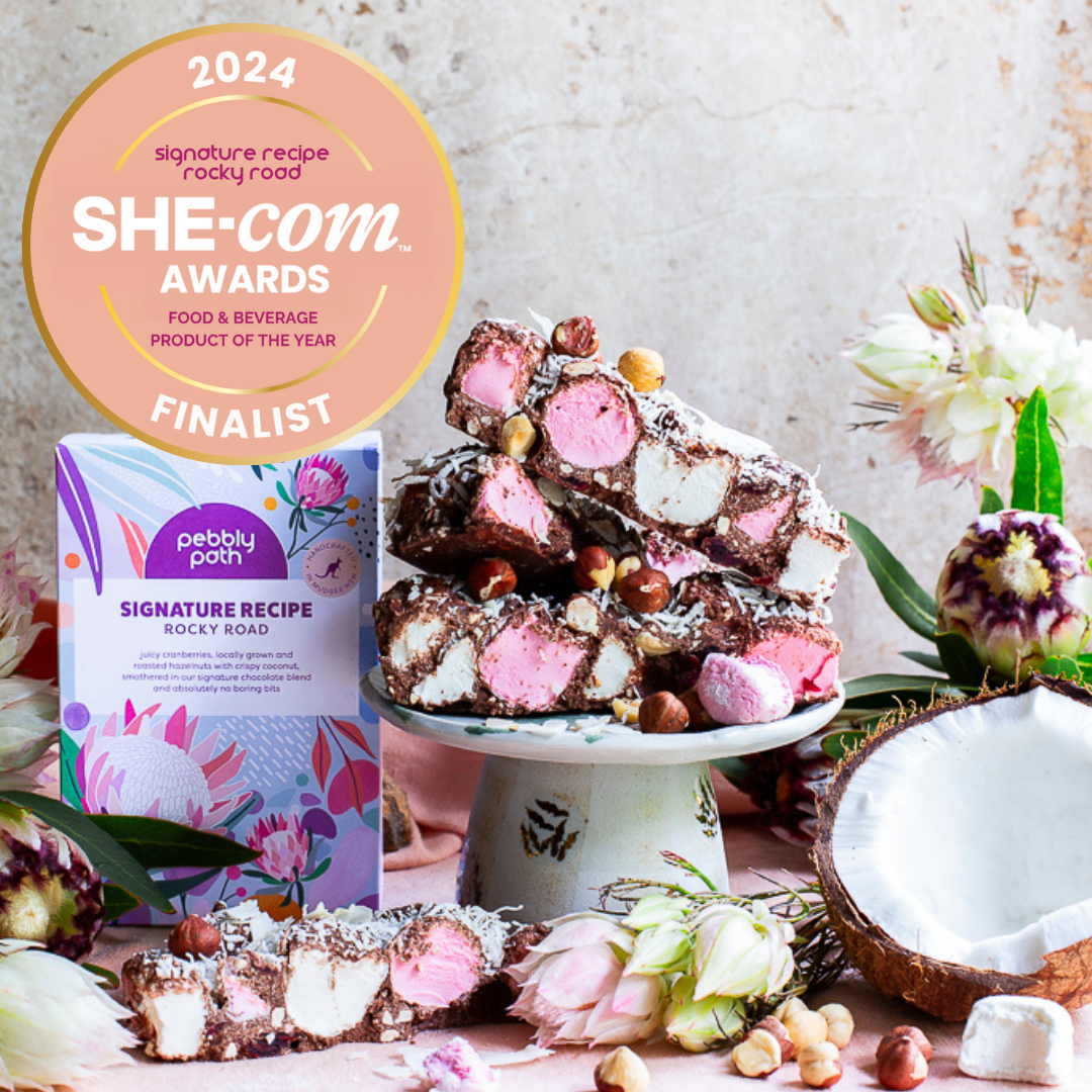 Pebbly Path personalised box of custom rocky road displayed alongside stacked rocky road pieces, marshmallows, hazelnuts and coconut, featuring a 2024 SHE-com Awards finalist badge in a styled product scene.