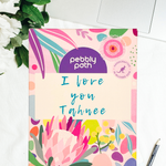 Pebbly Path personalised box of custom rocky road chocolate with a handwritten personalised message on floral gift packaging, displayed on a desk beside a laptop and pen.