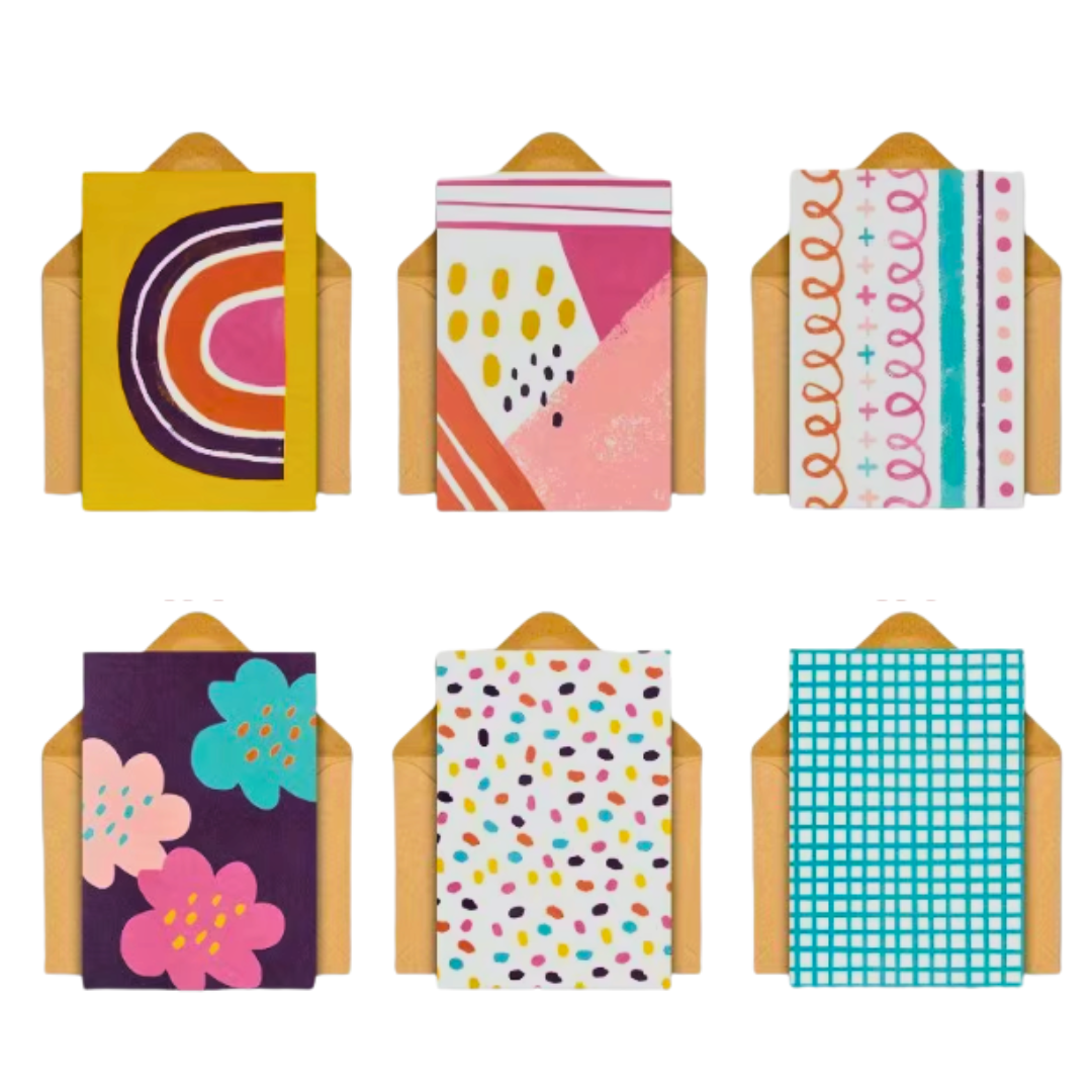 Pebbly Path greeting card assortment featuring six colourful abstract designs, including rainbow shapes, geometric patterns, floral illustrations, confetti-style dots, and a blue gingham pattern, displayed with kraft envelopes.