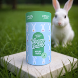 Pebbly Path Happy Easter Pick n Mix Rocky Road cylinder on a stone block in grass, light blue bunny design with green lid, white rabbit in soft focus behind, handmade in Mudgee, NSW.