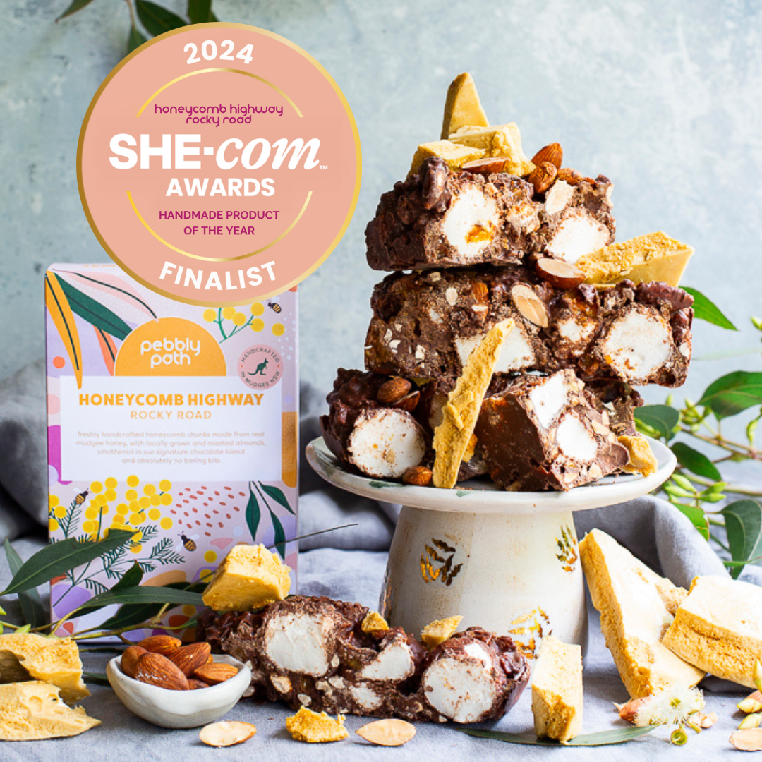Pebbly Path Honeycomb Highway Rocky Road displayed with stacked rocky road pieces, honeycomb chunks and almonds on a cake stand, featuring a 2024 SHE-com Awards Handmade Product of the Year finalist badge.