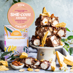 Pebbly Path Honeycomb Highway Rocky Road displayed with stacked rocky road pieces, honeycomb chunks and almonds on a cake stand, featuring a 2024 SHE-com Awards Handmade Product of the Year finalist badge.
