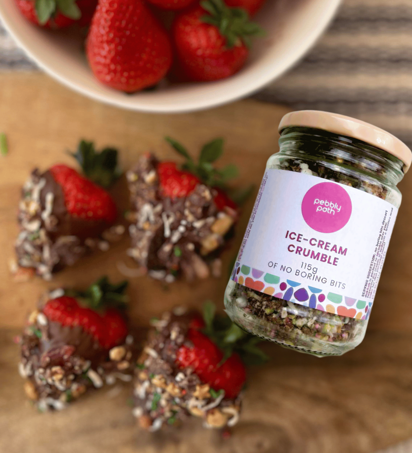 Pebbly Path ice-cream crumble jar beside fresh strawberries and chocolate treats, an Australian handmade chocolate topping for desserts.