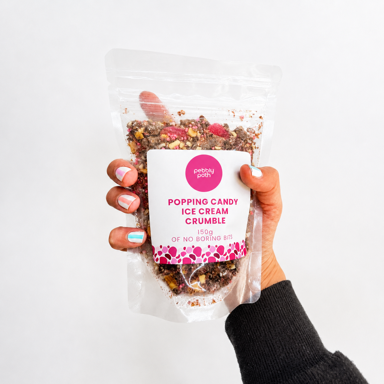 Pebbly Path Popping Candy Ice Cream Crumble in a clear 150g pouch, held in a hand with the colourful crumble mixture visible.