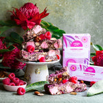 Pebbly Path Lovers Lane Rocky Road displayed with raspberry pieces, pink marshmallows and roasted almonds, styled with native flowers and branded packaging in a premium product display.