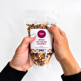 Pebbly Path Mixed Ice Cream Crumble Blend in a clear stand-up pouch, held in both hands with the front product label visible, showing the colourful crumble mix and resealable packaging.