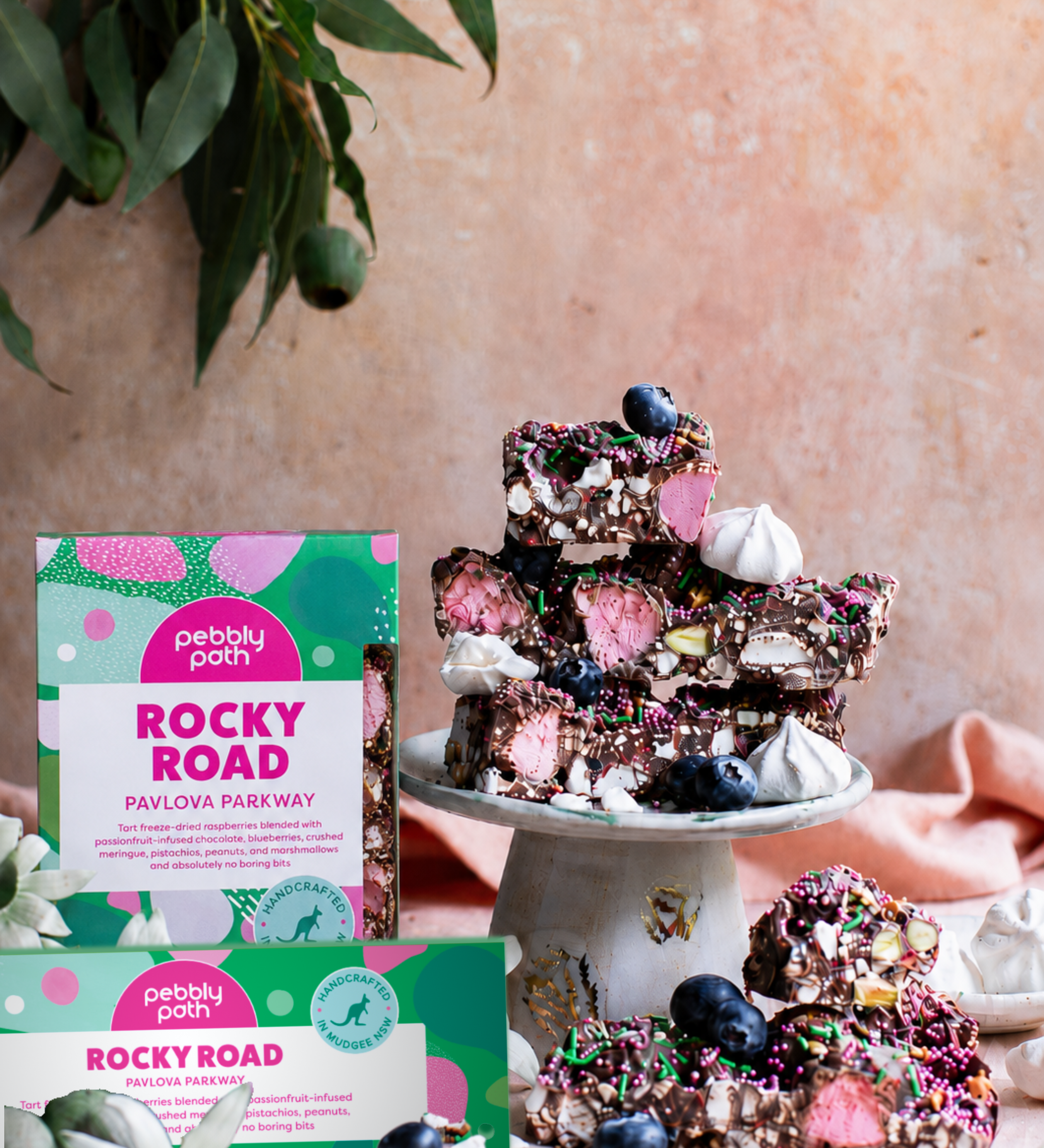 Pebbly Path Pavlova Parkway rocky road in 200g and 100g boxes, displayed with chocolate rocky road pieces topped with blueberries, marshmallows and colourful sprinkles.