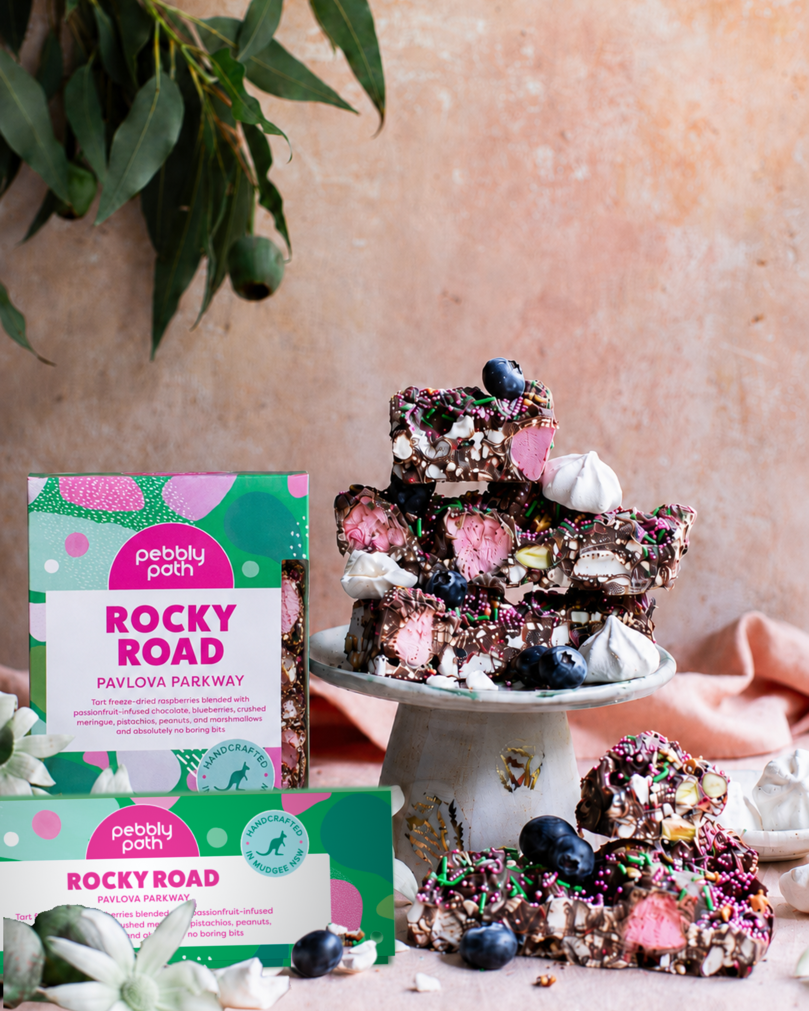 Pebbly Path Pavlova Parkway rocky road in 200g and 100g boxes, displayed with chocolate rocky road pieces topped with blueberries, marshmallows and colourful sprinkles.