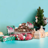 Pebbly Path Pavlova Parkway Rocky Road Christmas display with stacked rocky road pieces, festive packaging, meringue and holiday decorations beside illuminated ceramic houses and a mini Christmas tree