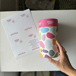 Pebbly Path PERSONALISED Rocky Road Pick n Mix Gift Cylinder held in hand beside a sheet of custom message labels, showing personalisation options for gifting and special occasions.