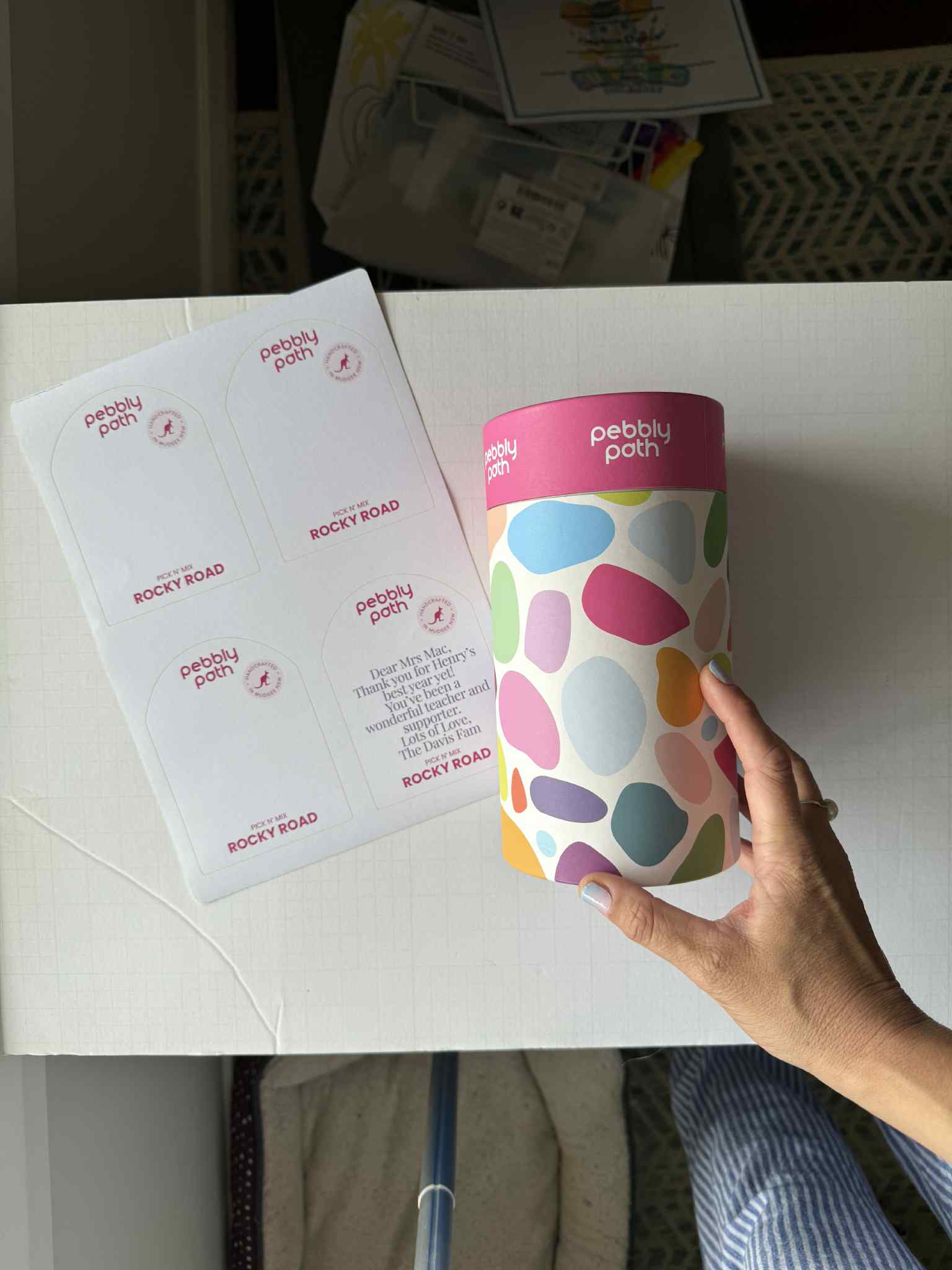 Pebbly Path PERSONALISED Rocky Road Pick n Mix Gift Cylinder held in hand beside a sheet of custom message labels, showing personalisation options for gifting and special occasions.