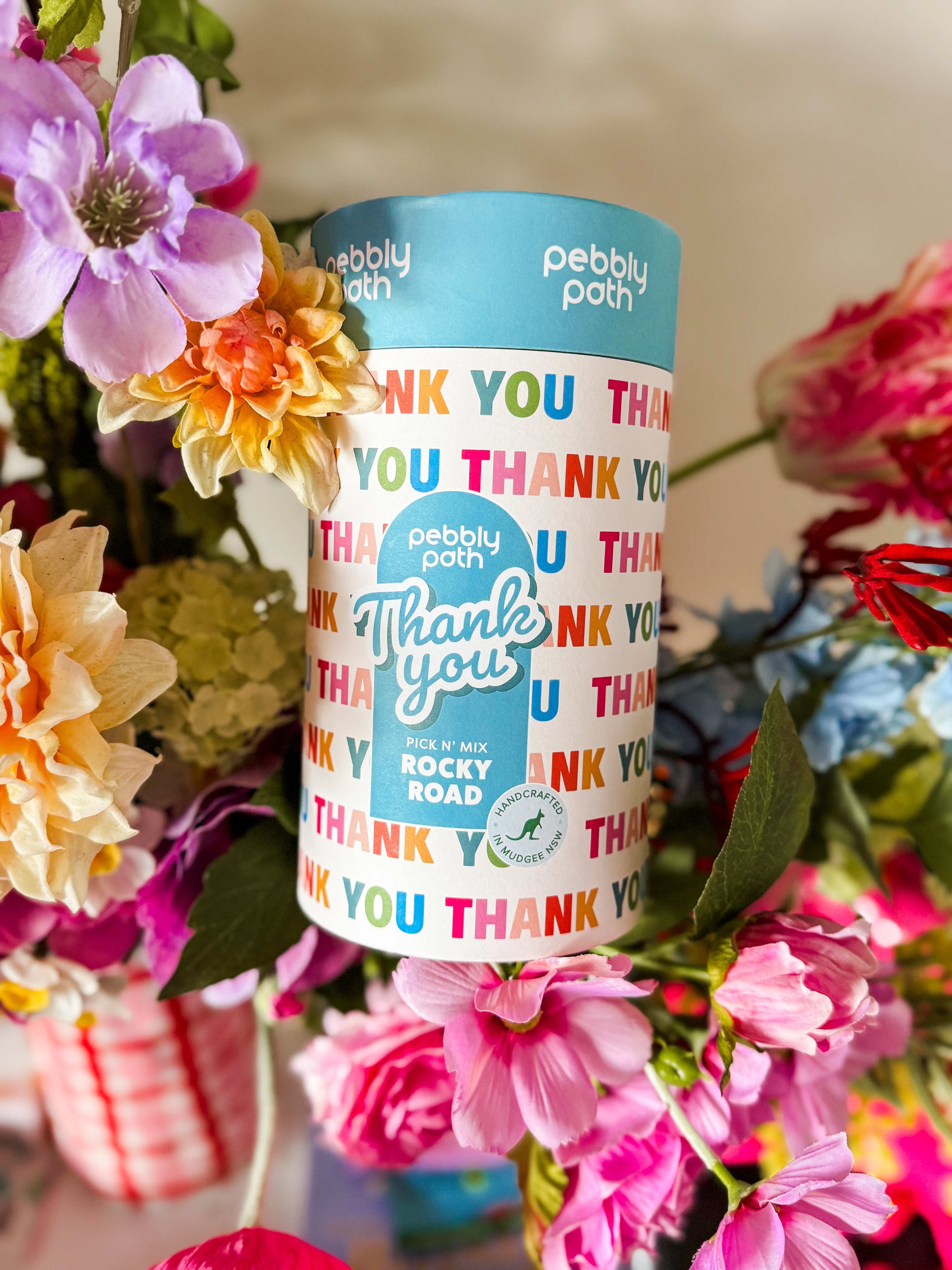 Pebbly Path Pick n Mix Rocky Road Cylinder with a Thank You design, surrounded by colourful flowers in a gift-style arrangement, showcasing a thoughtful appreciation gift for teachers, clients, colleagues, or special occasions.