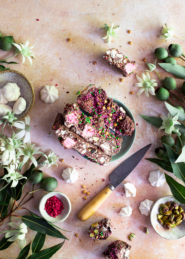 Pebbly Path Pavlova Parkway rocky road pieces arranged on a plate with passionfruit, meringue, pistachios and a knife.