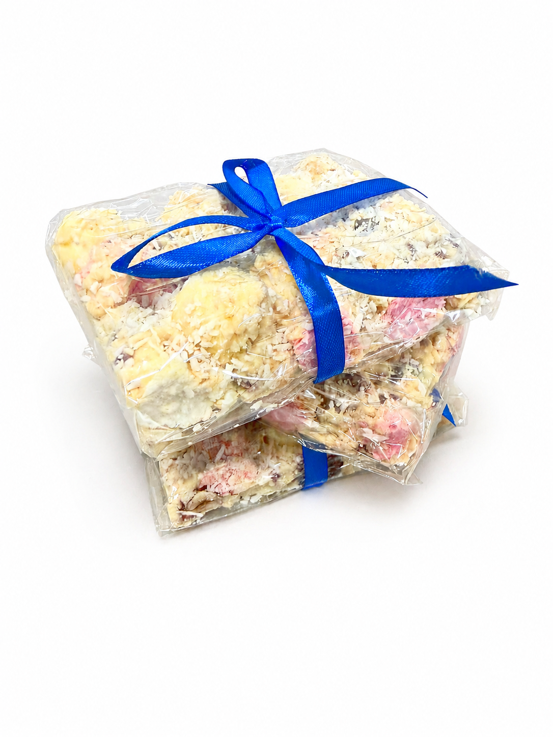 Pebbly Path White Chocolate Signature Recipe Rocky Road wrapped in clear packaging with a blue ribbon, shown from an angled view with stacked pieces, coconut flakes, and visible white chocolate coating.