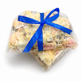 Pebbly Path White Chocolate Signature Recipe Rocky Road with two wrapped packs overlapping, tied with a blue ribbon and displayed on a white background with visible coconut flakes, marshmallow, and fruit pieces.