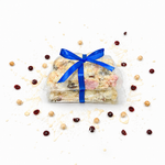 Pebbly Path White Chocolate Signature Recipe Rocky Road stacked pieces wrapped in clear packaging with a blue ribbon, displayed on a white background with coconut flakes, dried cranberries, macadamias, and white chocolate drizzle.