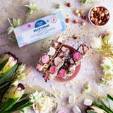 Pebbly Path Signature Recipe Rocky Road 100g bars styled with pink marshmallows, hazelnuts, coconut flakes, and branded packaging surrounded by native flowers and confectionery ingredients.