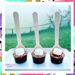 Pebbly Path Hot Chocolate Pops with marshmallows and colourful sprinkles displayed as a trio on a white tray with an outdoor countryside backdrop